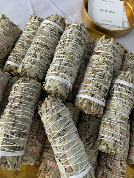 Hand-crafted Organic White Sage bundles, secured with white and pink cotton strings, arranged artistically, highlighting the natural texture and quality of the sage, used for spiritual purification and energy clearing.